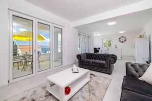 Uma sala de estar moderna com um sofá, uma mesa de centro e vista para o exterior através de grandes portas de correr de vidro.
