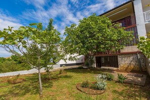Ein modernes Gebäude mit einer Stein-Fassade, einem roten Balkon und einem gepflegten Garten mit Bäumen und Pflanzen.