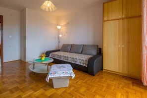 Ein Zimmer mit einer Couch, einem kleinen Tisch mit einer Vase, einer Stehlampe und einem Kleiderschrank.