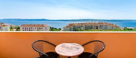A terrace with a round table and two chairs, overlooking a coastal town with buildings and a clear sky.