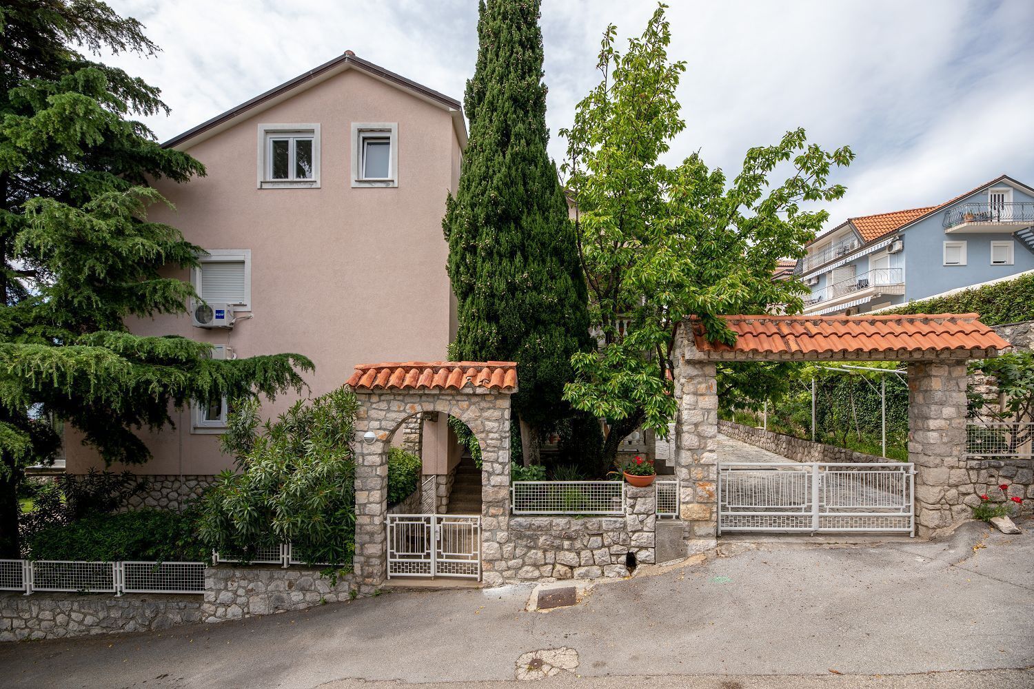 Un immeuble résidentiel avec une entrée en pierre, un toit recouvert de tuiles rouges et un grand arbre devant.