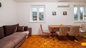 A modern living room with a brown sofa, a wooden dining table with chairs, and a large window with a view of buildings. - Tranquil studio apartment in a dream location just 250 metres from the sandy beach (Crikvenica)