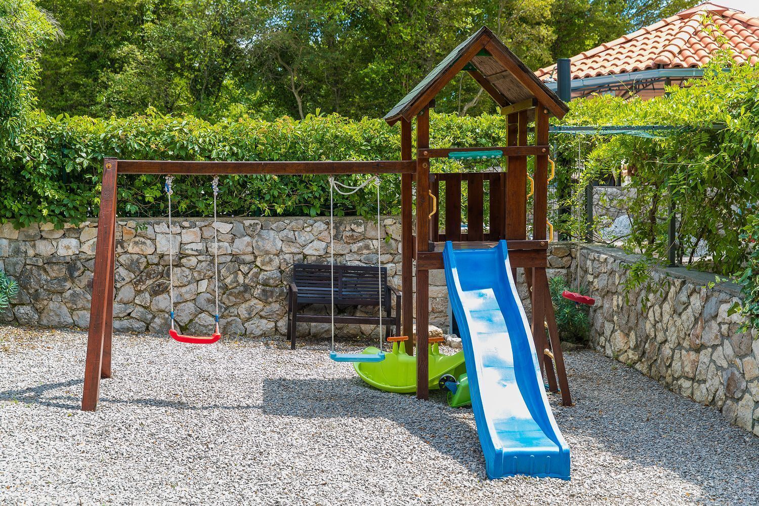 A wooden play structure with a slide, swings, and a bench.