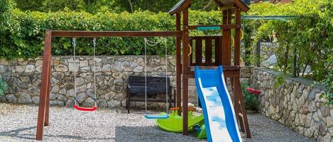 A wooden play structure with a slide, swings, and a bench.