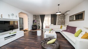 Een moderne woonkamer met een flatscreen televisie, witte banken, een leren relaxstoel en een stenen open haard.