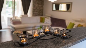 Een moderne keuken met een granieten aanrecht, vijf glazen kandelaars met kaarsen, een witte bank op de achtergrond en een hanglamp erboven.
