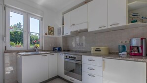 Una cocina moderna con armarios blancos, horno empotrado, cafetera y ventana con vistas a zonas verdes.