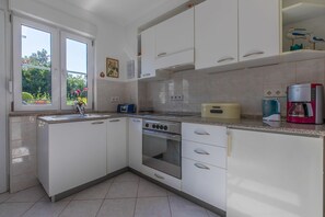 Eine moderne Küche mit weißen Schränken, einem Einbauofen, einer Kaffeemaschine und einem Fenster mit Blick auf Grünflächen.