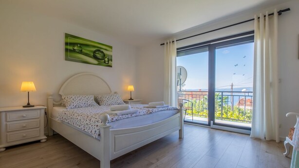 Un dormitorio con una cama, dos mesitas de noche con lámparas, un cuadro verde y un balcón con vistas.