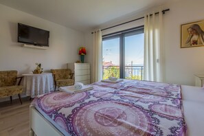 Ein Hotelzimmer mit einem Bett, zwei Stühlen, einem Fernseher, einem Fenster mit Vorhängen und einem Gemälde an der Wand.