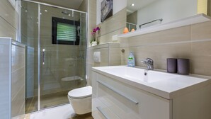 Un baño moderno con cabina de ducha de vidrio, un lavabo blanco y un inodoro.