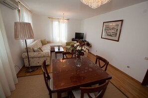 Un salon avec un canapé, une table à manger et des chaises, un téléviseur et un lustre.