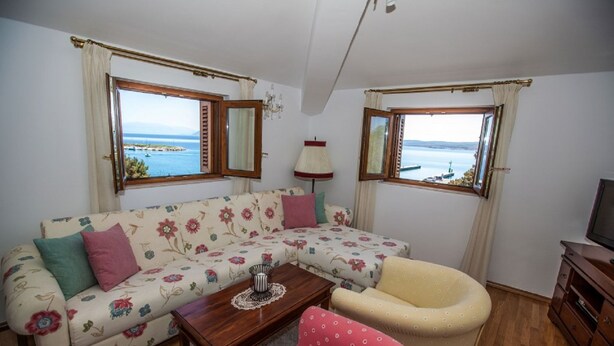 Ett vardagsrum med en soffa, en fåtölj och ett litet bord. Det finns två fönster med utsikt över havet.