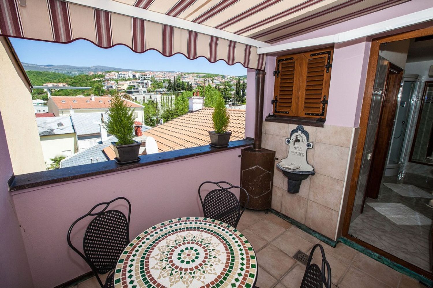 Ein Balkon mit Blick auf eine Stadtansicht, einem Kachelboden, zwei Stühlen, einem kleinen Tisch und einem dekorativen Wandbild.