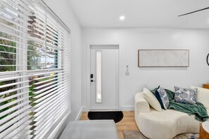 A modern living room with a white door, a sofa with patterned cushions, and a framed artwork on the wall. - 3 Miles to Atlantic Ave - Turtle Lane (Delray Beach)