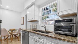 Eine moderne Küche mit weißen Schränken, Granit-Arbeitsplatten, einem eingebauten Backofen und einem Essbereich mit einem Glastisch und Stühlen.