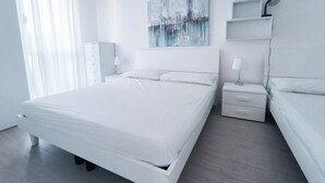 Un dormitori modern i minimalista amb un llit gran, taules de nit, una estant penjada a la paret i un quadre.