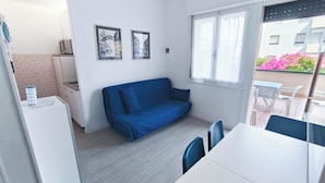 Un espai habitable compacte amb cuineta, un sofà blau, taula de dinar i vistes cap a l'exterior.