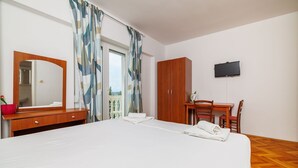 A hotel room with a bed, a wooden desk, a television, and a balcony with curtains. - Cosy studio apartment just 300 metres from the beach with sea view and parking space (Crikvenica)