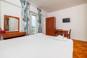 Ein Hotelzimmer mit Bett, einem Holztisch, einem Fernseher und einem Balkon mit Vorhängen.