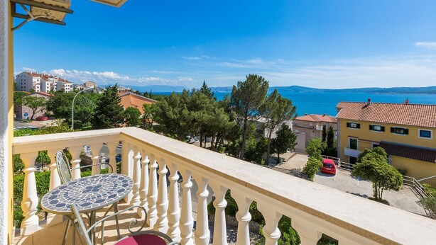 A balcony with a tiled table and chairs, overlooking a coastal town with buildings and trees. - Cosy studio apartment just 300 metres from the beach with sea view and parking space (Crikvenica)