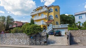 A multi-story yellow building with balconies, a stone wall, and a parked car. - Cosy studio apartment just 300 metres from the beach with sea view and parking space (Crikvenica)