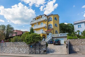 Ein mehrstöckiges gelbes Gebäude mit Balkonen, einer Steinmauer und einem geparkten Auto.