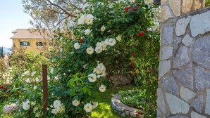 A garden with a stone wall and climbing roses. - Cosy studio apartment just 300 metres from the beach with sea view and parking space (Crikvenica)