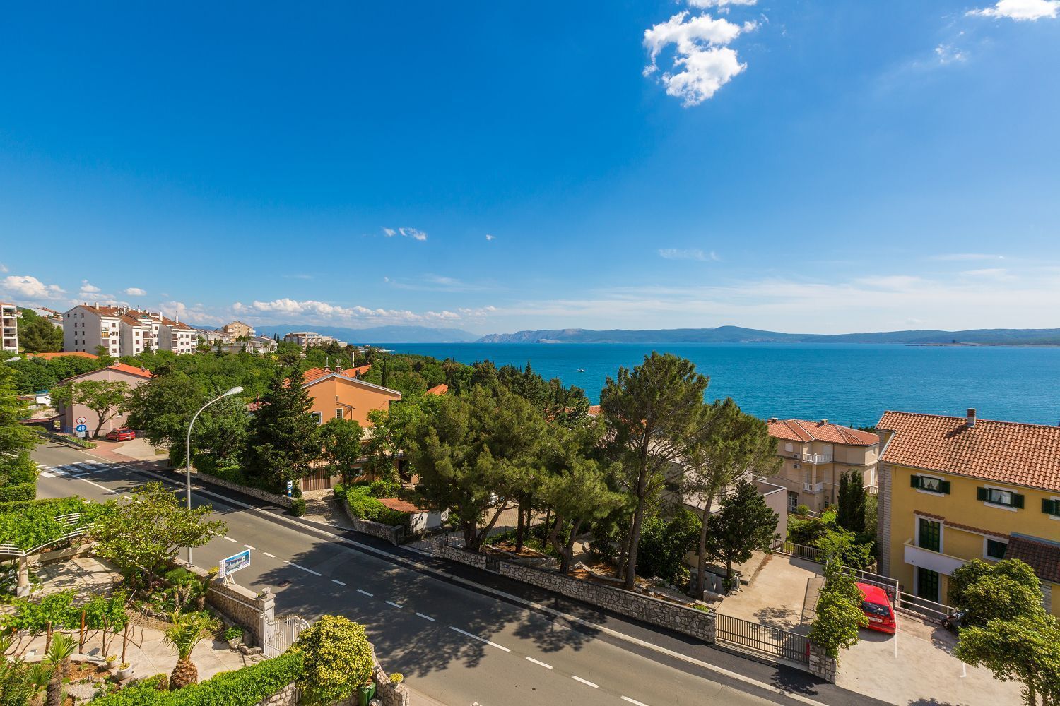 A coastal street with buildings, trees, and a clear view of the sea.
