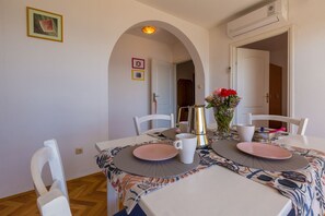 Ein Essbereich mit Tisch für zwei Personen, weißen Stühlen, einer Blumenvase und einer Kaffeekanne.