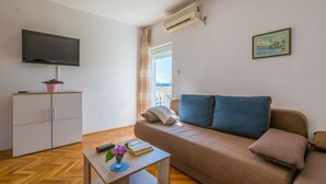 Un salon comprenant un canapé, un téléviseur, une petite table avec un vase et un meuble.