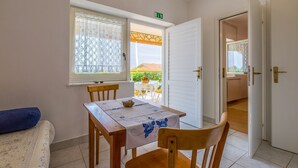 Een klein eethoekje met een tafel en stoelen, een raam met een decoratief gordijn en een open deur die leidt naar een terras.