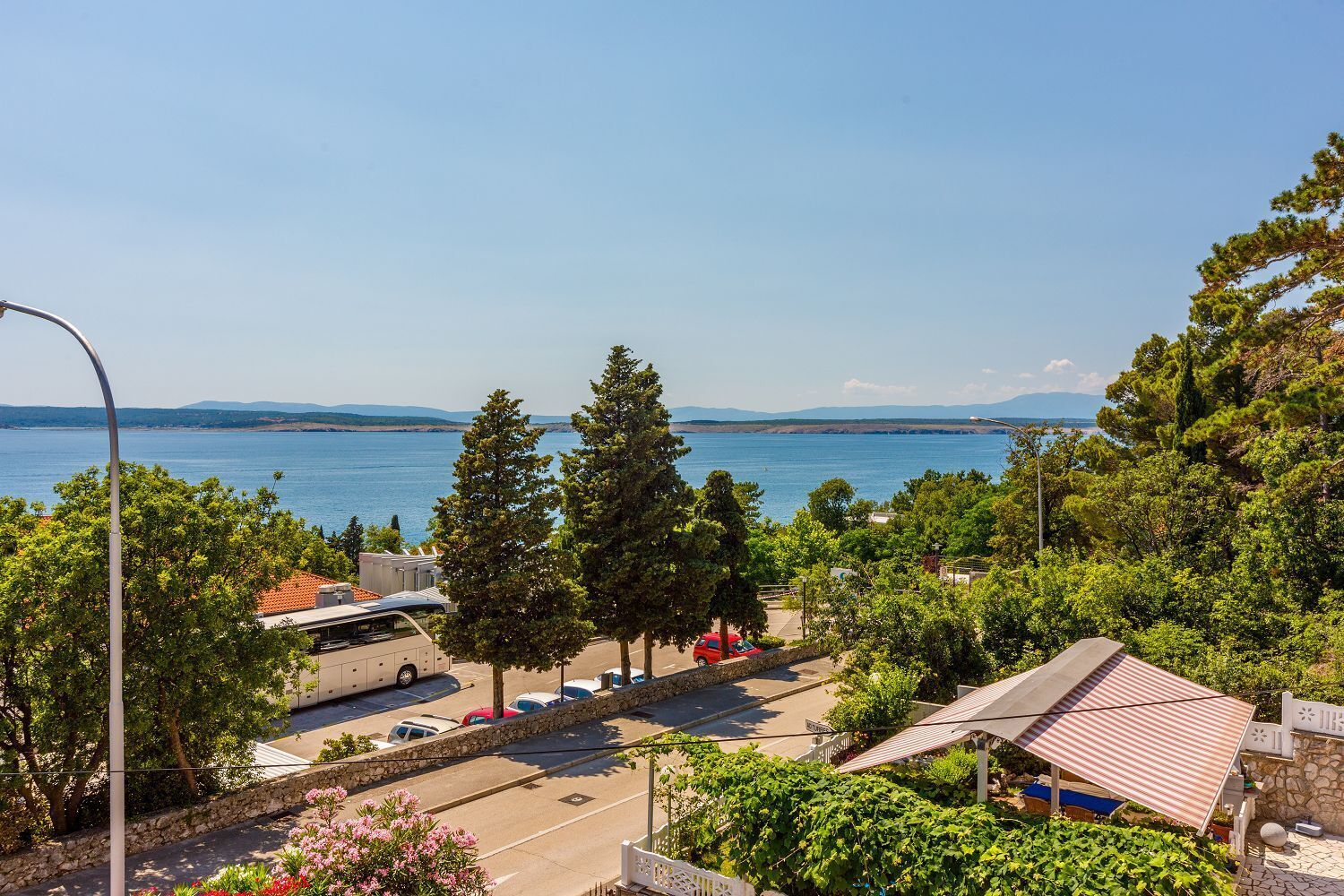 Vista costeira com área de estacionamento, árvores e céu claro.