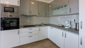 Een moderne keuken met witte kasten, een inbouwoven, een magnetron, een koffiezetapparaat en een spoelbak.