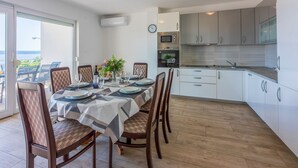 Een eetruimte met een tafel voor zes personen, omringd door houten stoelen. Daaraan grenst een keuken met moderne apparatuur en witte kasten.