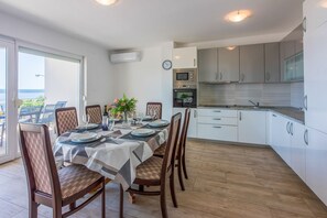 Ein Essbereich mit einem für sechs Personen gedeckten Tisch, umgeben von Holzstühlen. Anliegend eine Küche mit modernen Geräten und weißen Schränken.