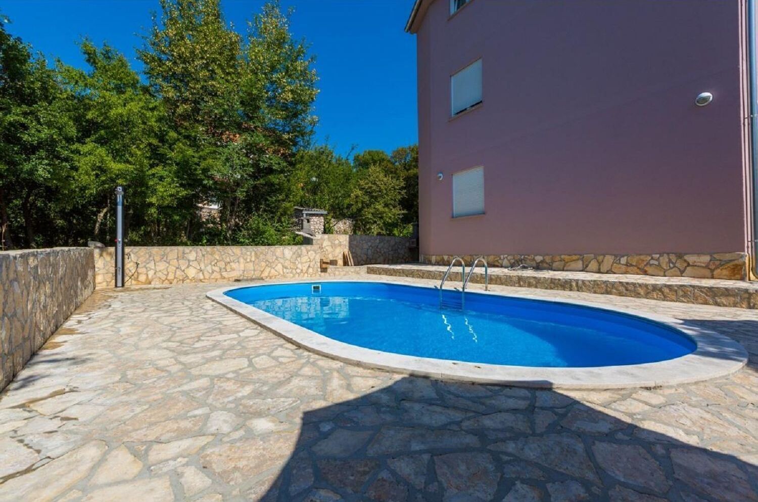 A swimming pool with stone tiles, a stone wall, and a building in the background.
