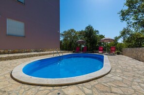 A swimming pool with a stone deck, surrounded by a stone wall and a building with a window.