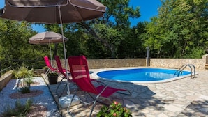 A swimming pool with lounge chairs and umbrellas, surrounded by stone tiles and greenery. - Special apartment with pool, barbecue area, washing machine, sea view, air conditioning (Grižane)