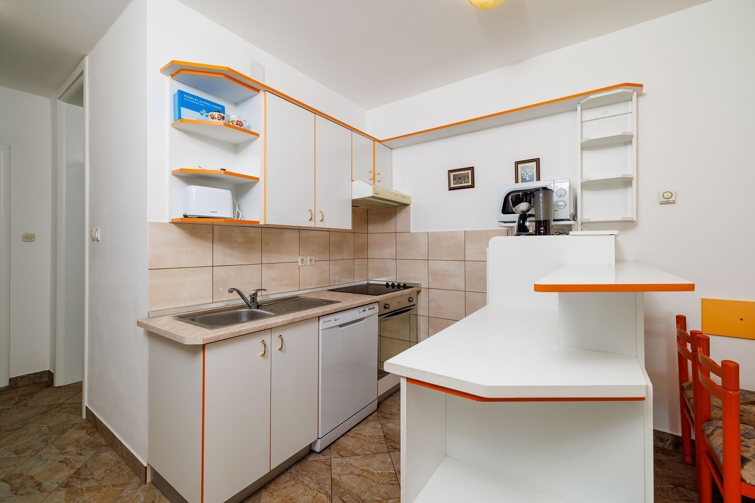 A compact kitchen with white cabinets, a built-in oven, a dishwasher, and a coffee machine.