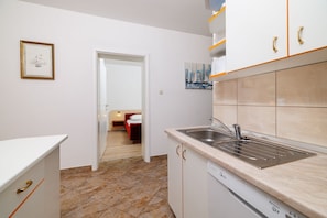 Una cocina compacta con un lavamanos y lavavajillas, y una cama roja en la habitación contigua.