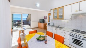 Una cocina compacta con comedor, un televisor pequeño y vista al mar a través de una puerta corredera.