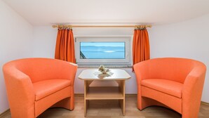 Una habitación con dos sillones naranjas, una mesita blanca y un ventanal con cortinas.