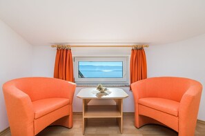 Ein Zimmer mit zwei orangefarbenen Sesseln, einem kleinen weißen Tisch und einem Fenster mit Vorhängen.