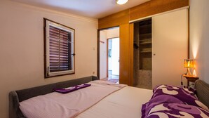 Ein Schlafzimmer mit Bett, einem Fenster mit Jalousien, einem Kleiderschrank und einem Nachttisch mit Lampe.