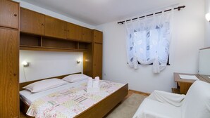 Ein Schlafzimmer mit einem hölzernen Bett, einem Nachttisch, einem Stuhl und einem Fenster mit Vorhang.
