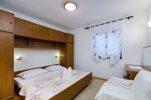 A bedroom with a wooden bed, a bedside table, a chair, and a window with a curtain. - Quiet apartment with Mediterranean terrace, barbecue area, parking space, air conditioning, WiFi (Crikvenica)