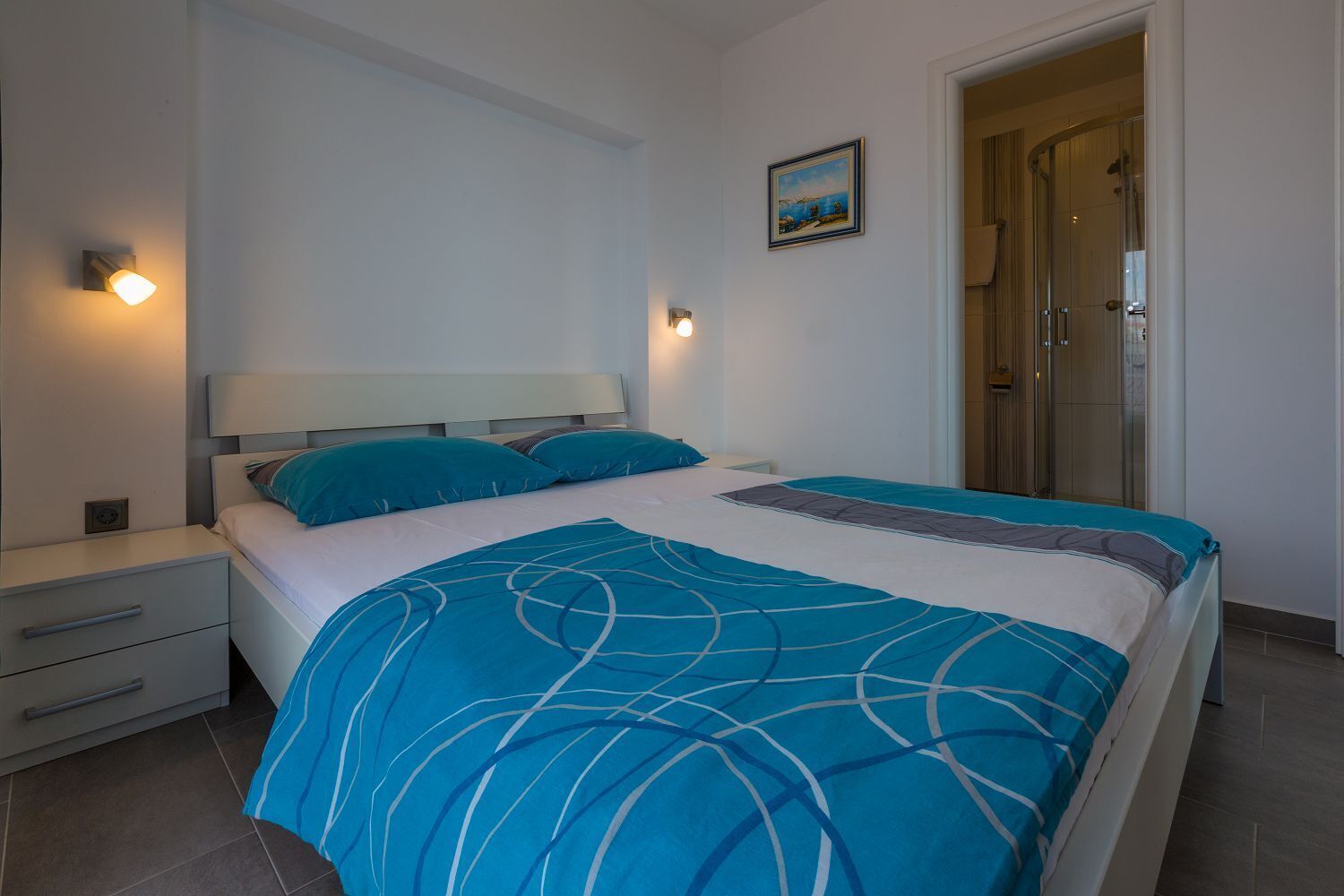 Une chambre à coucher comprenant un lit, des tables de chevet, une commode, un tableau au mur et un espace douche.