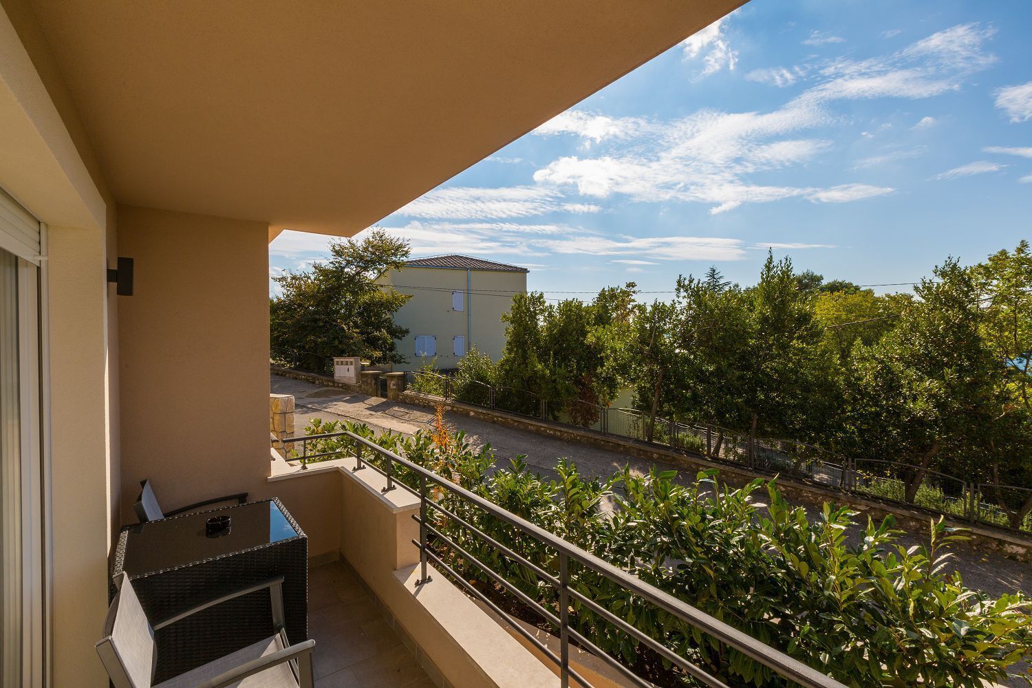 Een balkon met een barbecue, uitzicht op een straat en een gebouw op de achtergrond.