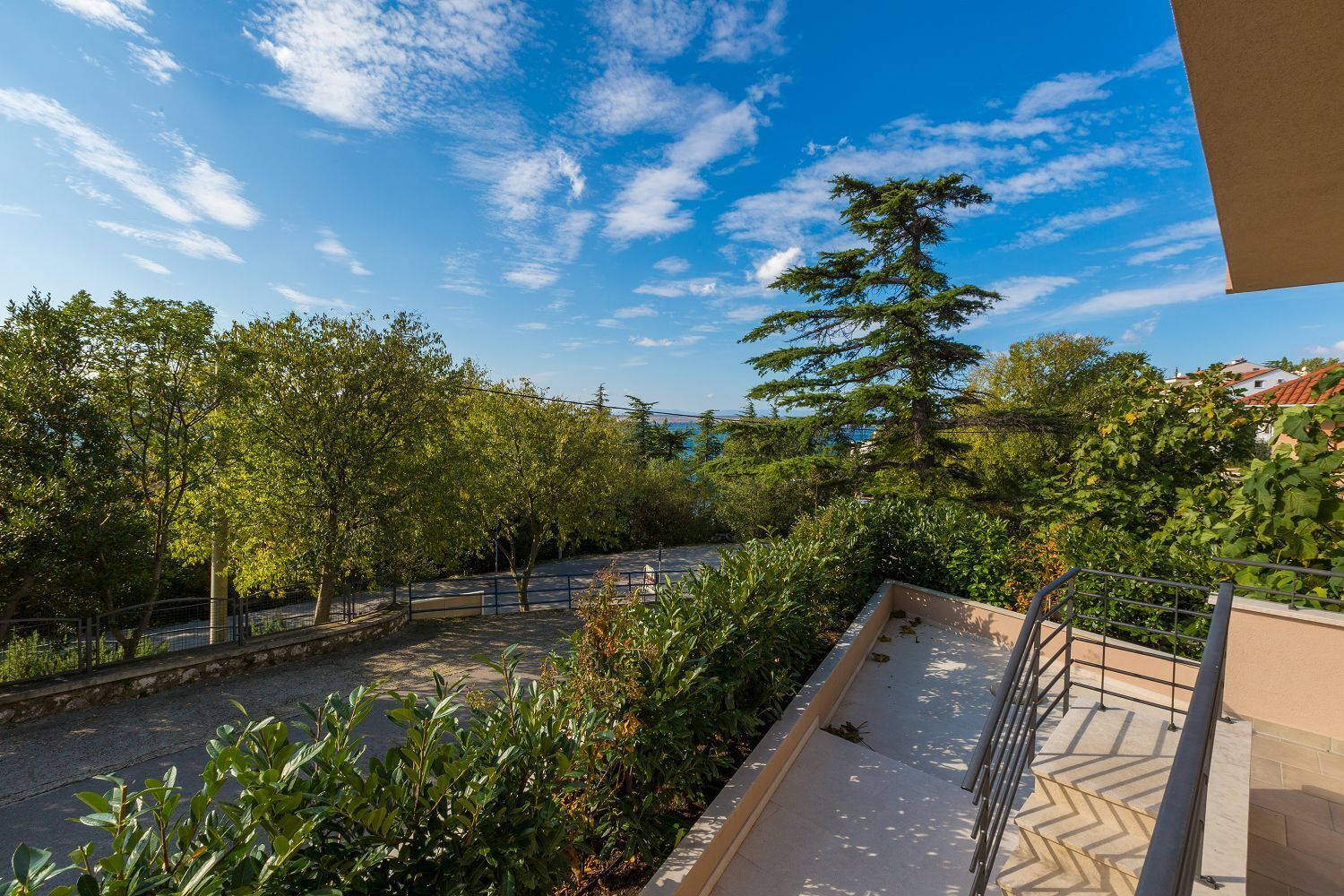 Un balcon donnant sur une rue bordée d’arbres et sur un ciel bleu dégagé.